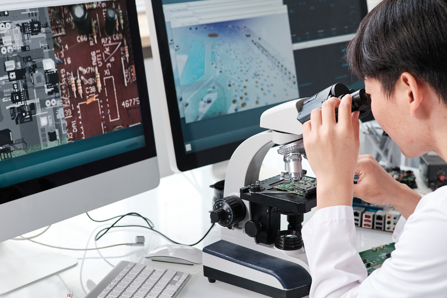 Person looking at a electronic board with a microscope Person looking at a electronic board with a microscope