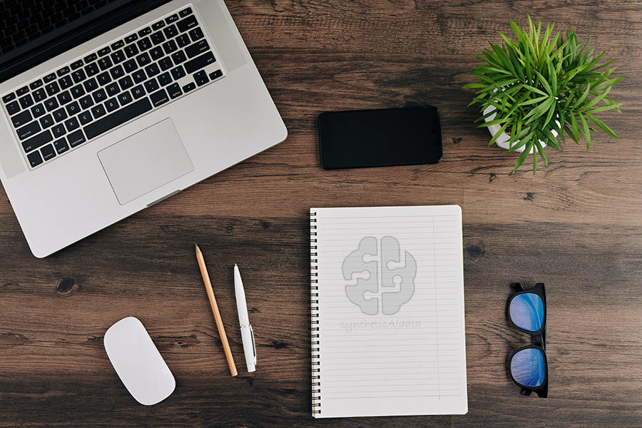 A desk with a laptop, mouse, phone, glasses and a notebook with syntheticAIdata written on it